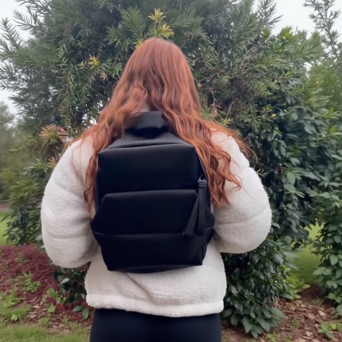 Person wearing a black backpack with a blurred natural background